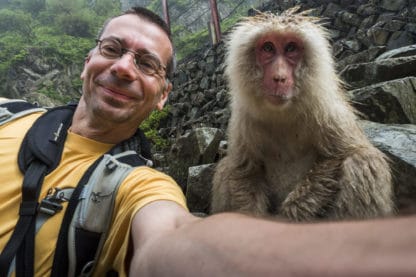 Adrian Rohnfelder nimmt ein Selfie mit einem Affen auf. Im Hintergrund eine Steinmauer. Der Fotograf lächelt, der Affe hat ein ausdrucksloses Gesicht. Reisefotografie.