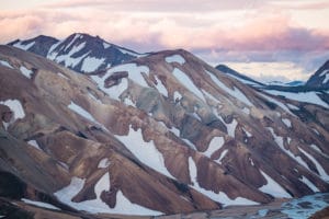 Eine Berglandschaft die teilweise mit Schnee bedeckt ist. Im Hintergrund die von der Sonne rosa angestrahlten Wolken und der Himmel in Abendstimmung. Islands Süden im Spätsommer. Vulkan, Landschaft und Eis.