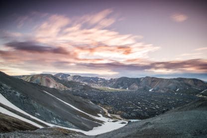 Landschaftsbild aus Island. Schwarze Berge und Hänge, teilweise mit Schnee bedeckt. Der Himmel ist rosa und lila und ein paar weiße Wolken werden von der Sonne angestrahlt. Islands Süden im Spätsommer. Vulkan, Landschaft und Eis!